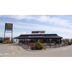 En McDonalds-restaurant med udendørs siddepladser, en drive-thru-bane og et højt skilt med McDonalds-logoet nær parkeringspladsen.